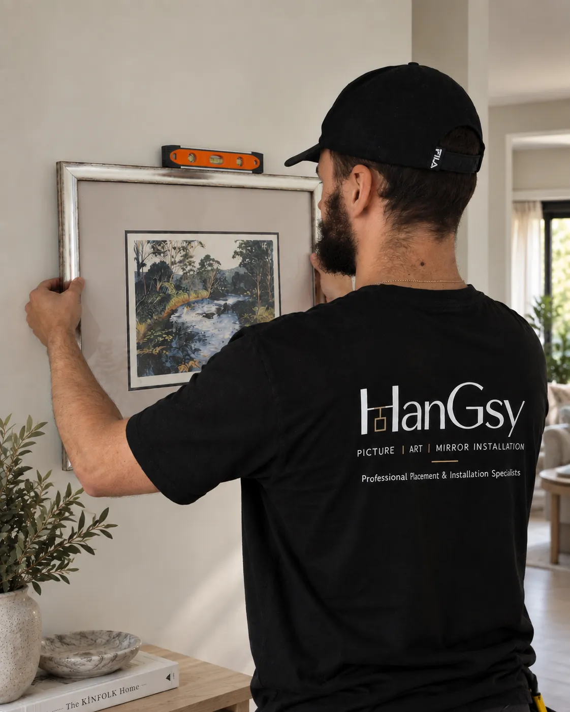 Jacob positioning and levelling a framed artwork during a HanGsy installation